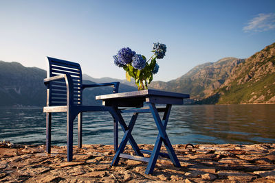 Empty chairs and table by lake against sky