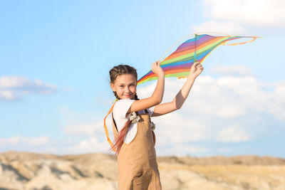 A girl in summer dress launches a kite into the sky in the wild.