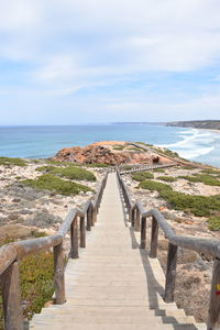 Walkway leading towards sea against sky