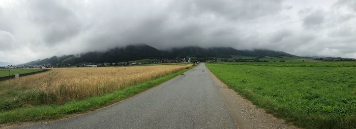 Panoramic view of road amidst field against sky