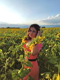 Portrait of young woman standing amidst flowering plants on field against sky