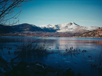 Scenic view of lake by snowcapped mountains against clear sky
