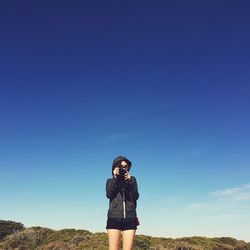 Portrait of young woman standing against clear blue sky