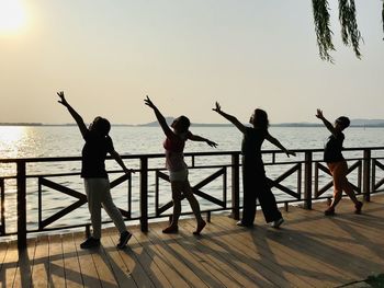 People dancing by railing over sea against sky