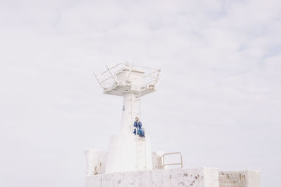 Low angle view of woman photographing while sitting on lookout tower against sky