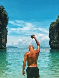 Full length of shirtless man standing in sea against sky