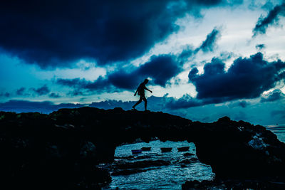 Silhouette man standing on rock against sky