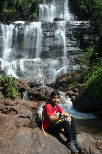 Rear view of man sitting against waterfall
