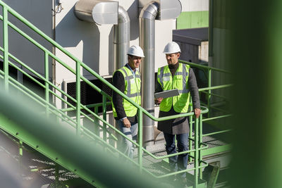 Engineers wearing hardhat discussing at recycling plant on sunny day