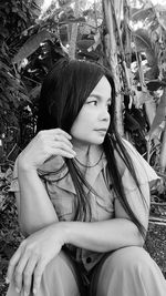 Woman looking away while sitting against plants