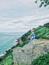 Man standing on rock by sea against sky