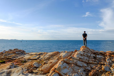 Man standing on rock by sea against sky