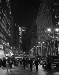 People walking on illuminated street in city at night