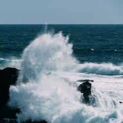 Waves splashing on sea against clear sky