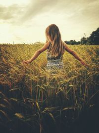 Rear view of girl standing in wheat field against sky