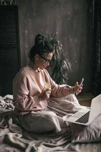 Midsection of woman using mobile phone while sitting on bed at home