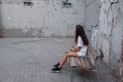 Side view of woman sitting on wall