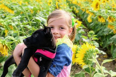 Portrait of smiling cute girl holding dog while standing on field