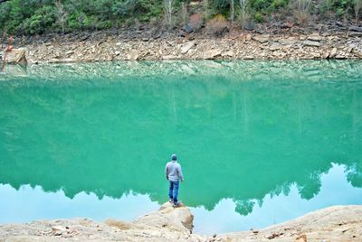 Rear view of man standing on rock by lake