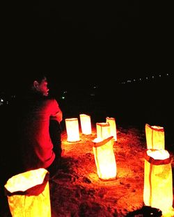 Midsection of man at illuminated beach against sky at night