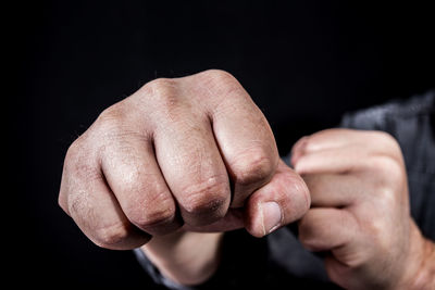Cropped hands of man punching over black background