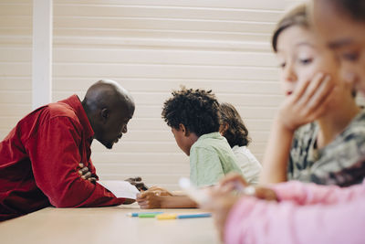 Teacher guiding students in learning through digital tablet at desk in classroom