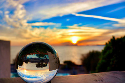 Close-up of crystal ball on glass against sunset sky