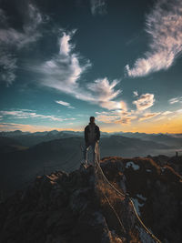 Rear view of man standing on rock against sky during sunset