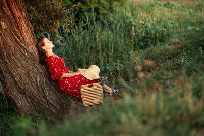 Side view of woman relaxing by tree