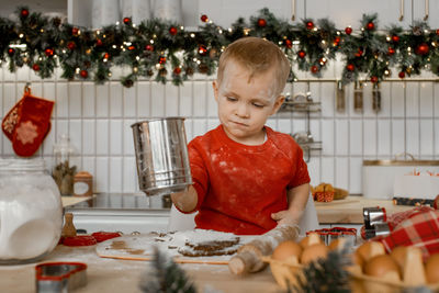 Cute little boy is very busy sifting flour through a sieve on the dough in christmas kitchen
