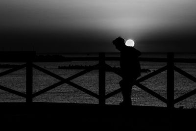 Silhouette man standing by railing against sea during sunset