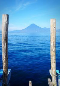 Wooden posts in sea against blue sky