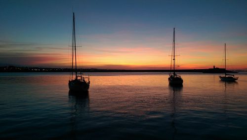 Sailboats in sea at sunset