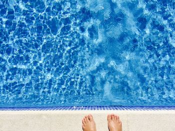 Low section of person standing at poolside on sunny day