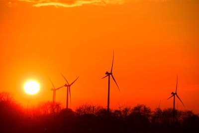 Silhouette wind turbines on field against orange sky