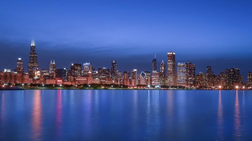 Illuminated urban skyline by lake michigan at dusk