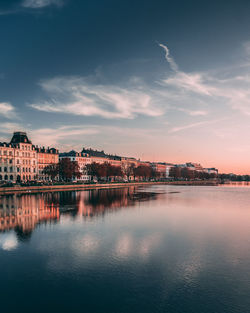 Scenic view of river by buildings against sky during sunset