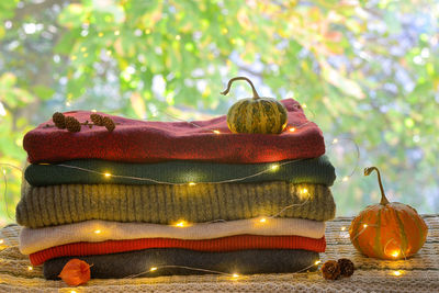 Close-up of illuminated lights on warm clothing and pumpkins and pine cones over table