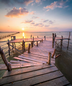 Wooden pier over sea against sky during sunset