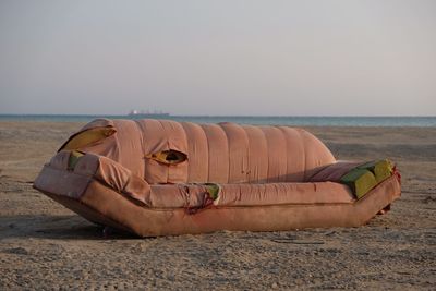 Old sofa at beach against clear sky