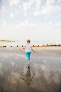 Rear view of mid adult women walking at beach against sky