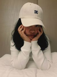 Portrait of young woman sitting against wall at home