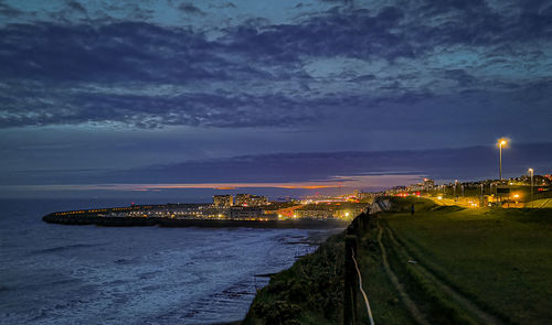 Illuminated buildings by sea against sky at night