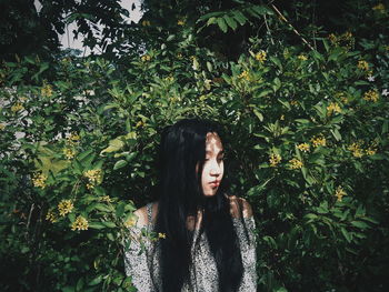 Young woman looking away while standing against plants