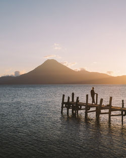 Man on pier over sea against sky during sunset