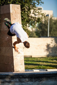 Young man doing stunt on retaining wall in park