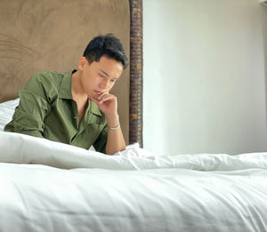 Young man looking away while relaxing on bed at home
