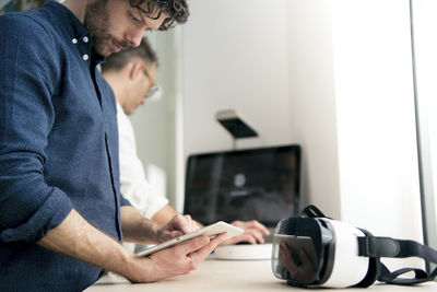 Engineer using tablet computer while colleague using computer in office