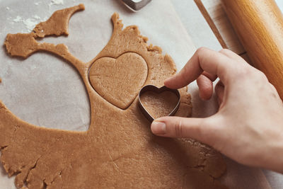 Making gingerbread cookies in shape of a heart for valentines day. woman hand use cookie cutter.