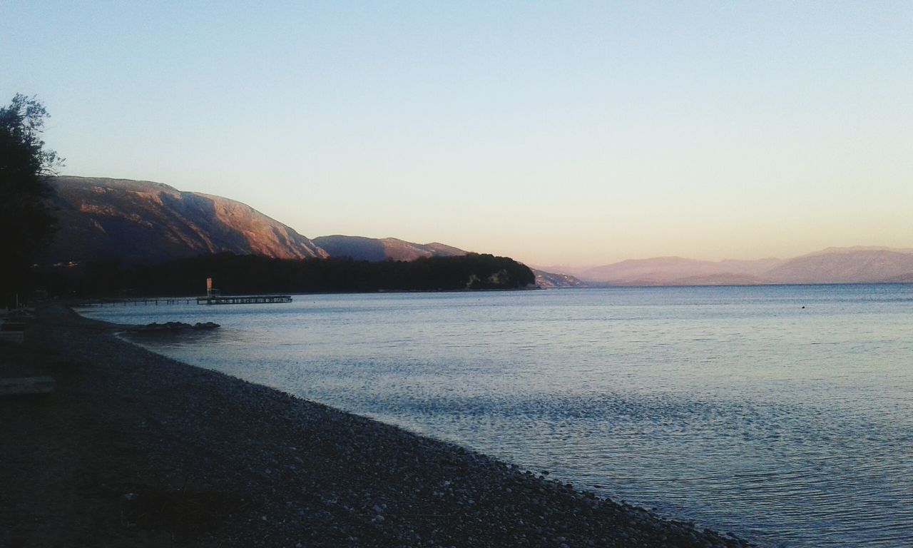 clear sky, water, mountain, tranquil scene, copy space, scenics, tranquility, beauty in nature, sea, nature, mountain range, idyllic, beach, coastline, lake, outdoors, non-urban scene, sunset, no people, calm